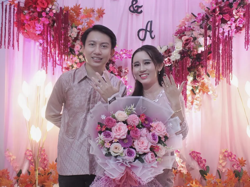 Pasangan memperlihatkan cincin tunangan sambil membawa buket.