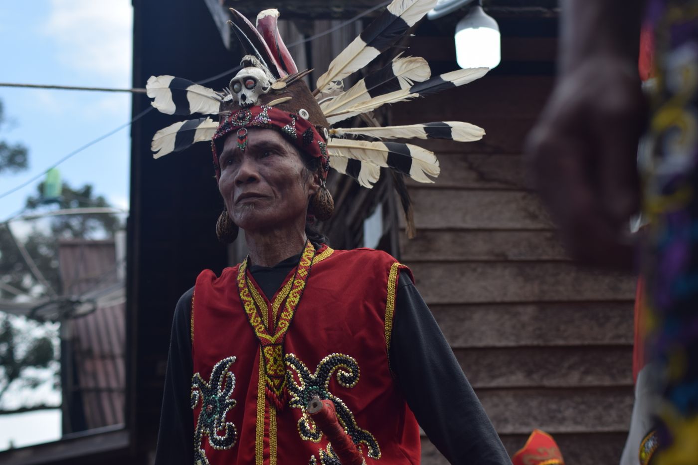 Tetua berbusana adat merah-hitam dengan mahkota bulu